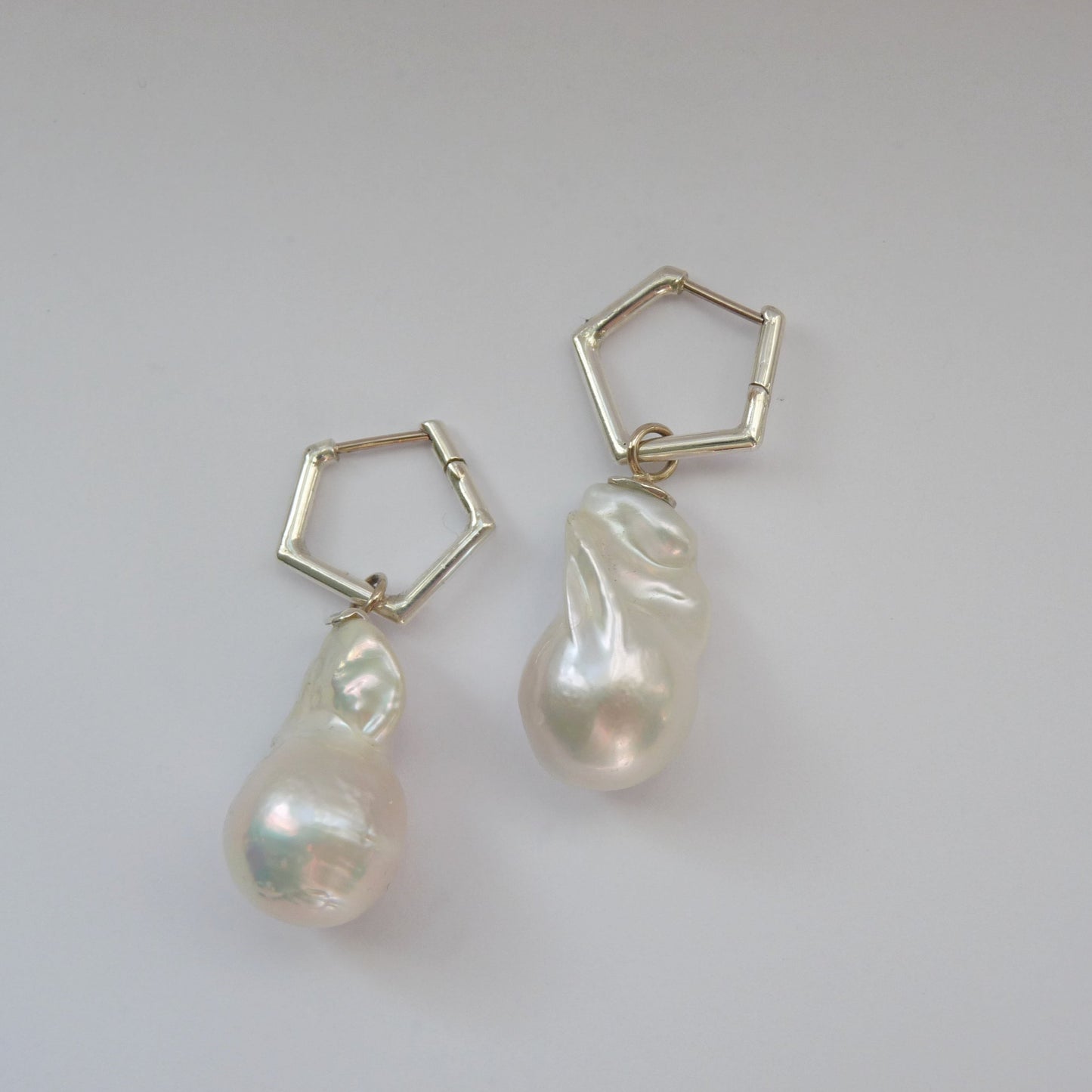 Des boucles d'oreilles au design géométrique associées à des perles baroques naturelles offrent une harmonie entre modernité et nature